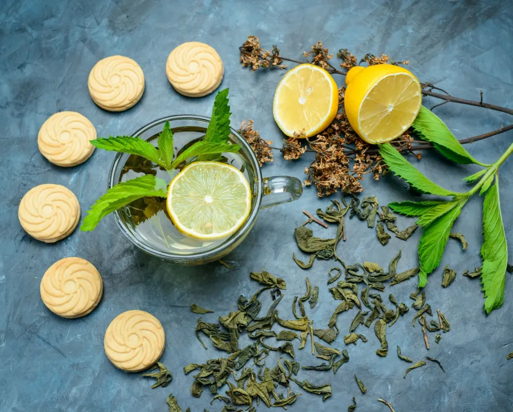 the-dans-une-tasse-de-citron-biscuits-menthe-herbes-sechees-a-plat-sur-une-surface-bleue.webp